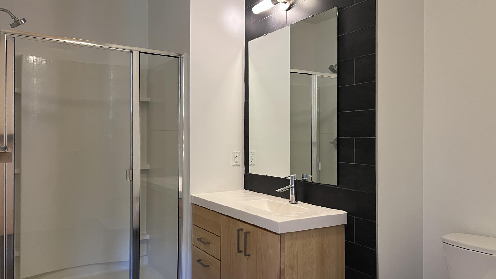 One bedroom apartment bathroom with glass shower enclosure and modern lighting, and tile flooring and wet wall at SEVEN27 in downtown Madison